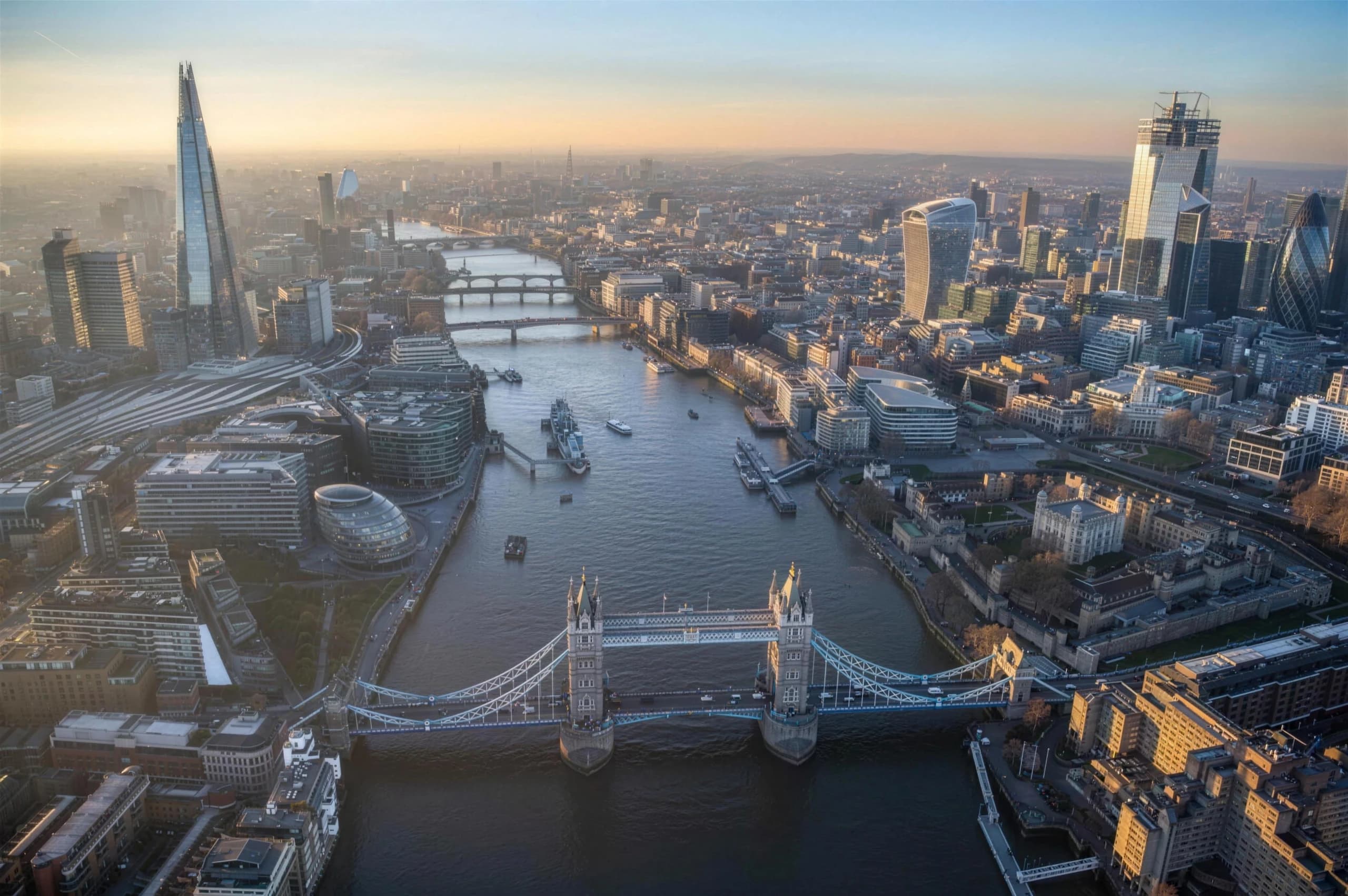 Aerial view of London — Tower Bridge over the Thames, with the Shard and the City skyline in golden light.